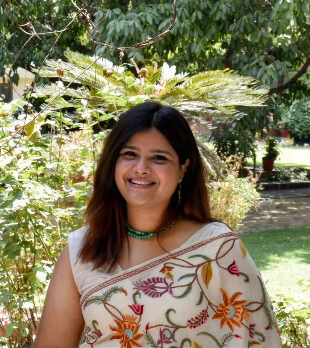 Woman standing in front of a decorative wooden gate with greenery in the background