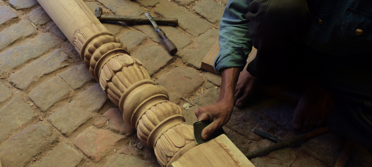 Wooden carvings being worked on by a craftsman with tools on a brick floor.